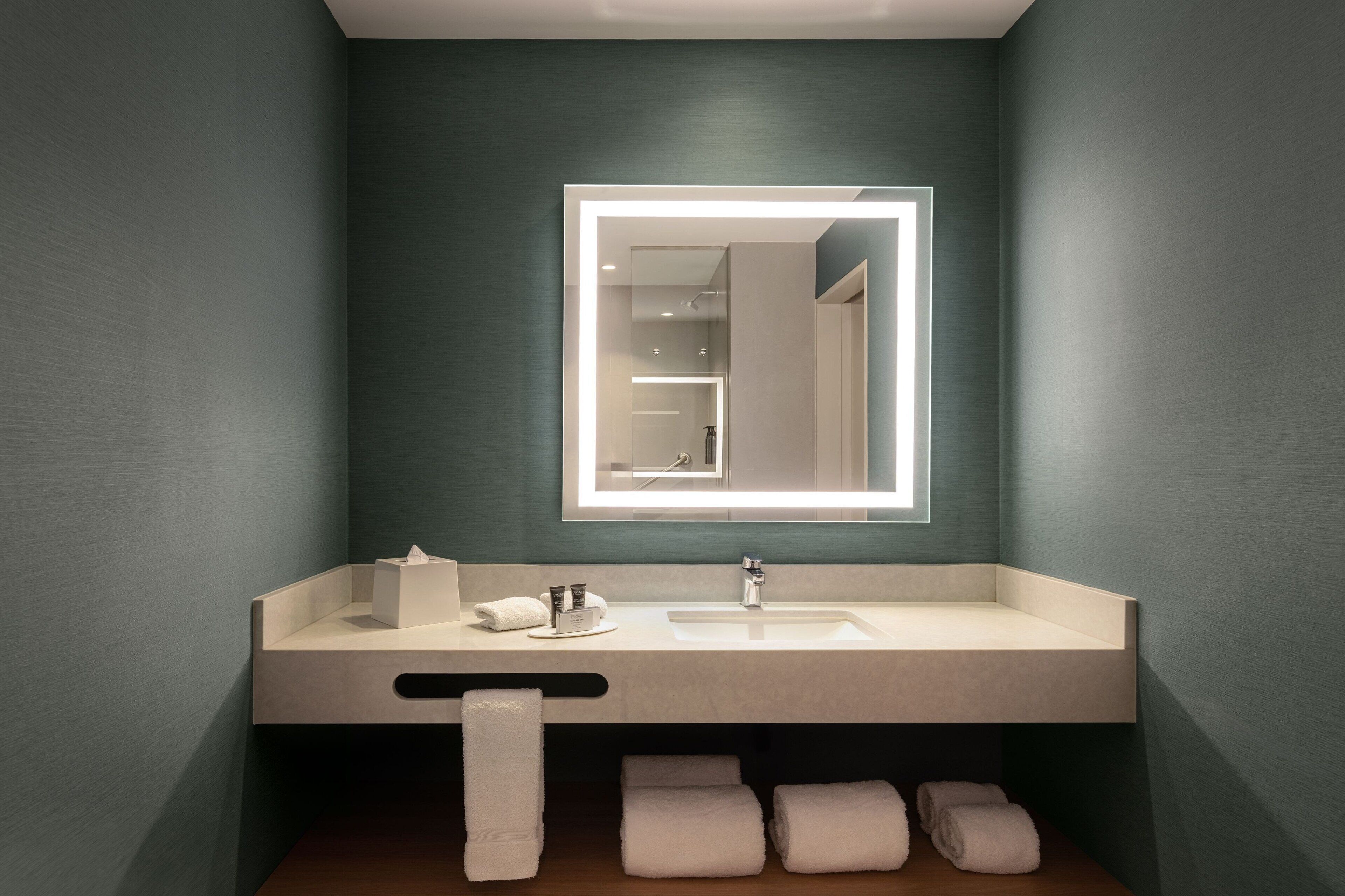 A modern bathroom with a large mirror, a sink, and multiple towels.