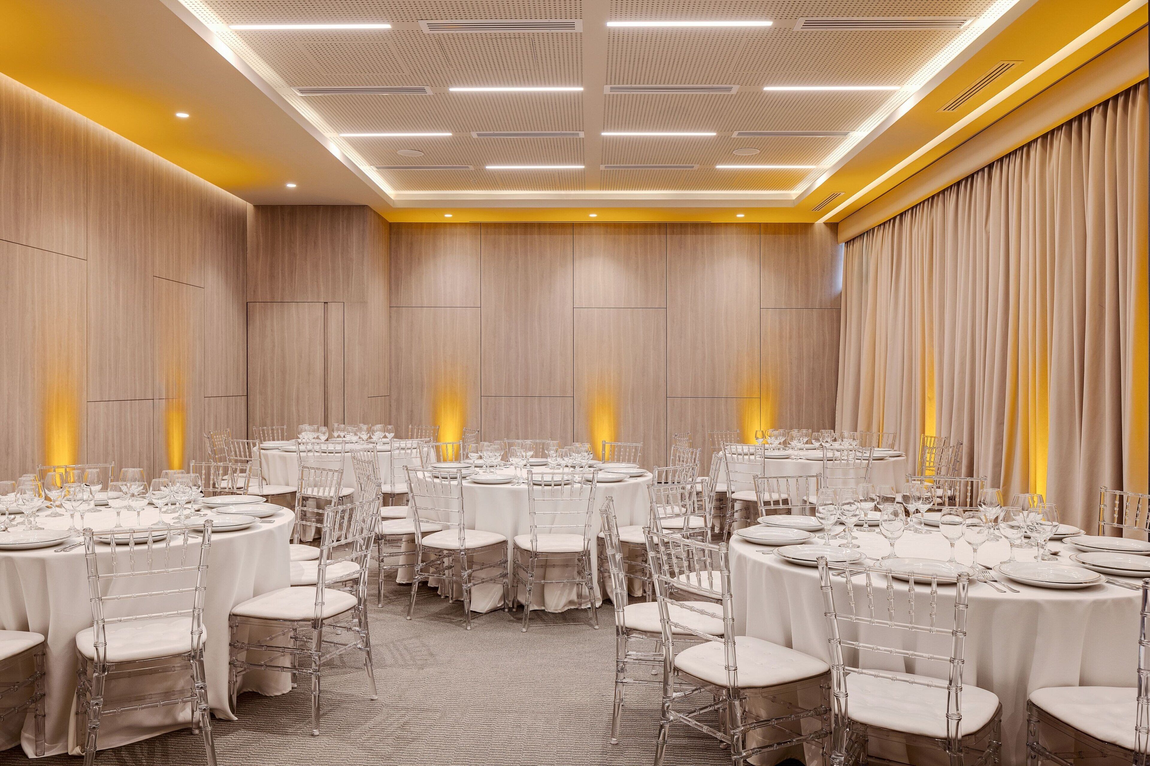 Un salón de banquetes con varias mesas redondas dispuestas para comer, equipado con sillas y vajilla.