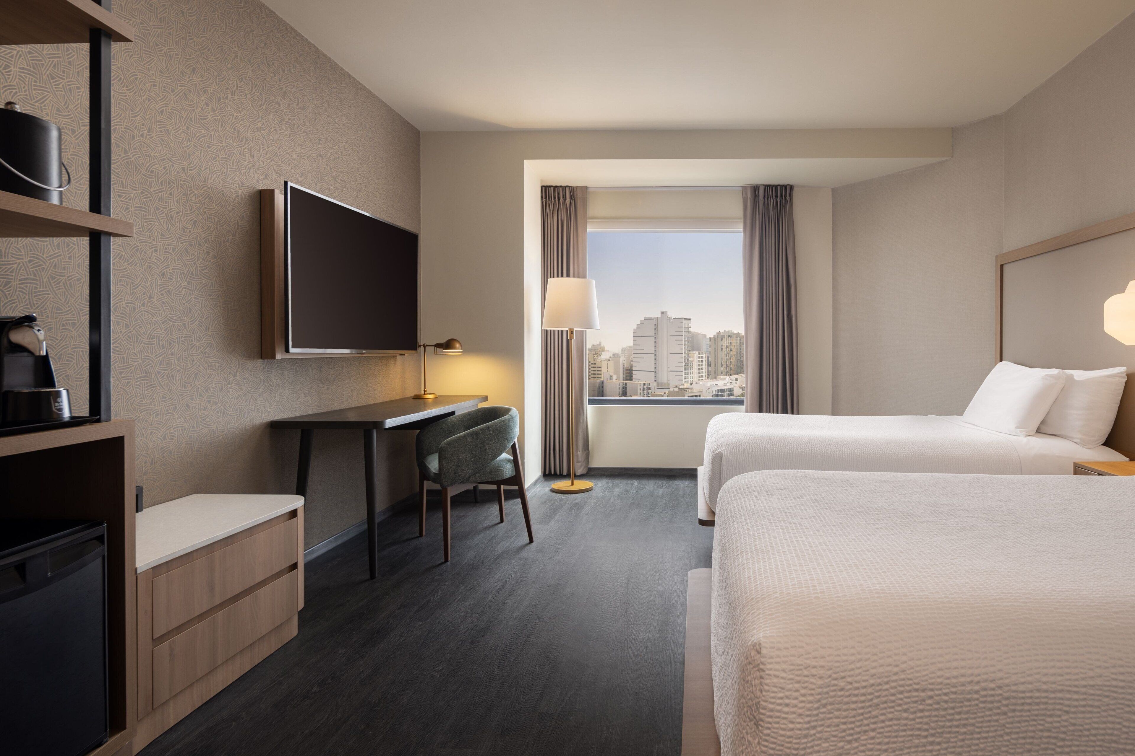 Quarto de hotel com escrivaninha, duas camas, televisão e vista para a cidade.