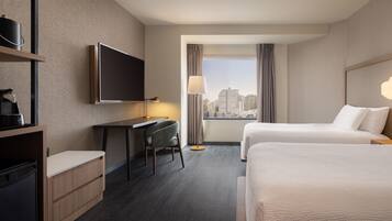 Quarto de hotel com escrivaninha, duas camas, televisão e vista para a cidade.