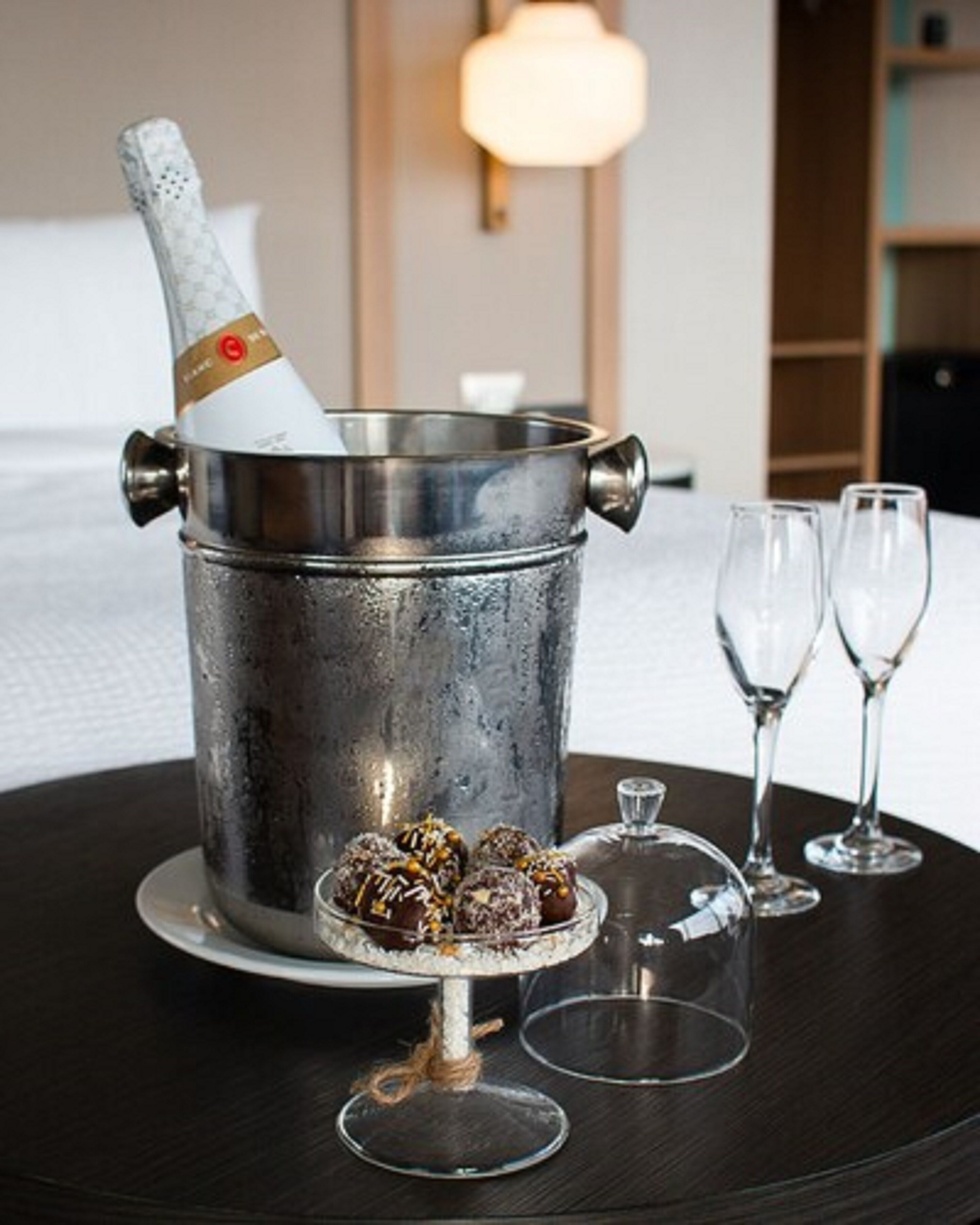 Un cubo metálico para champán con una botella, dos copas de vino vacías y bombones de chocolate sobre una bandeja.