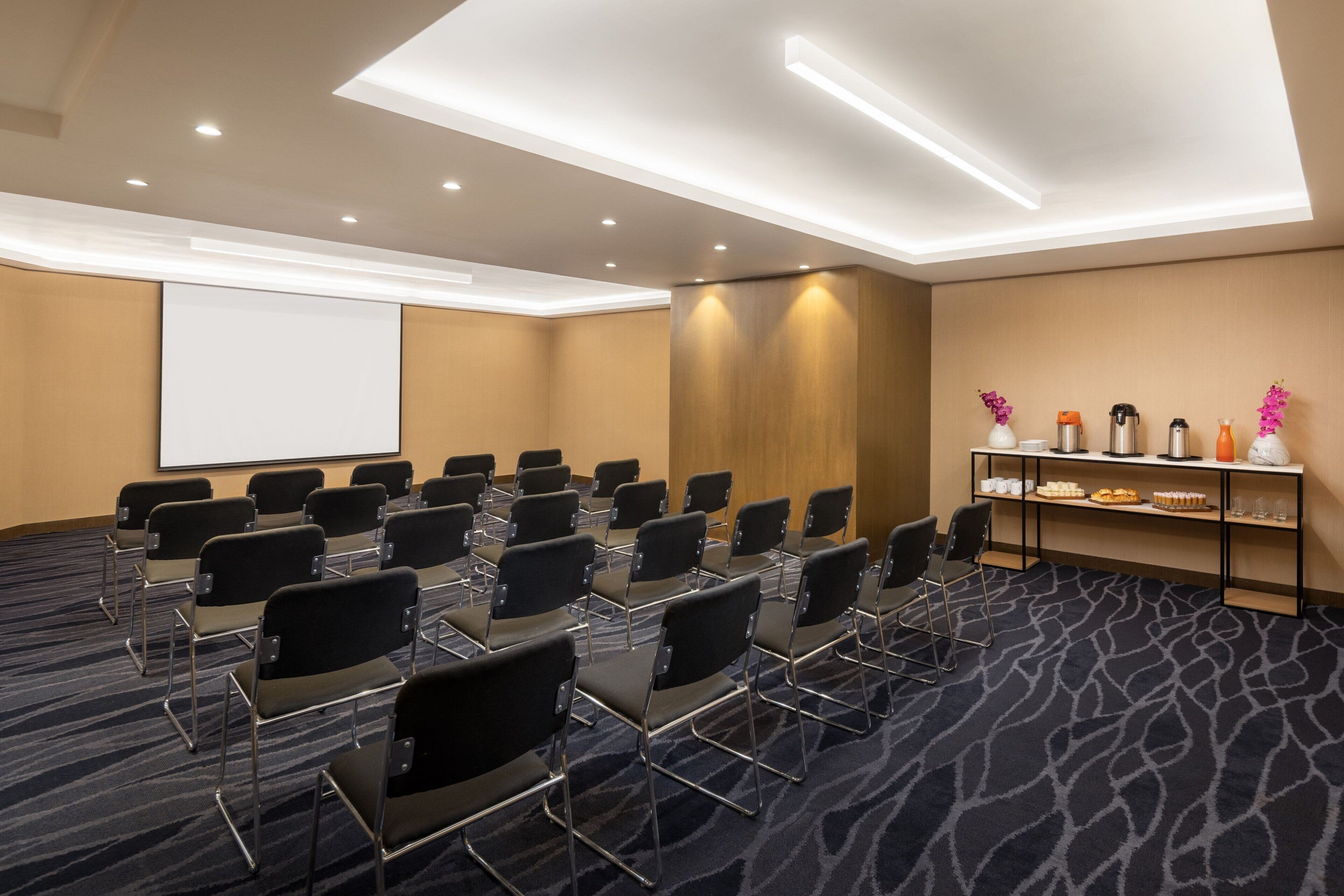 A conference room with rows of chairs, a projector screen, and a buffet table with food and drinks.