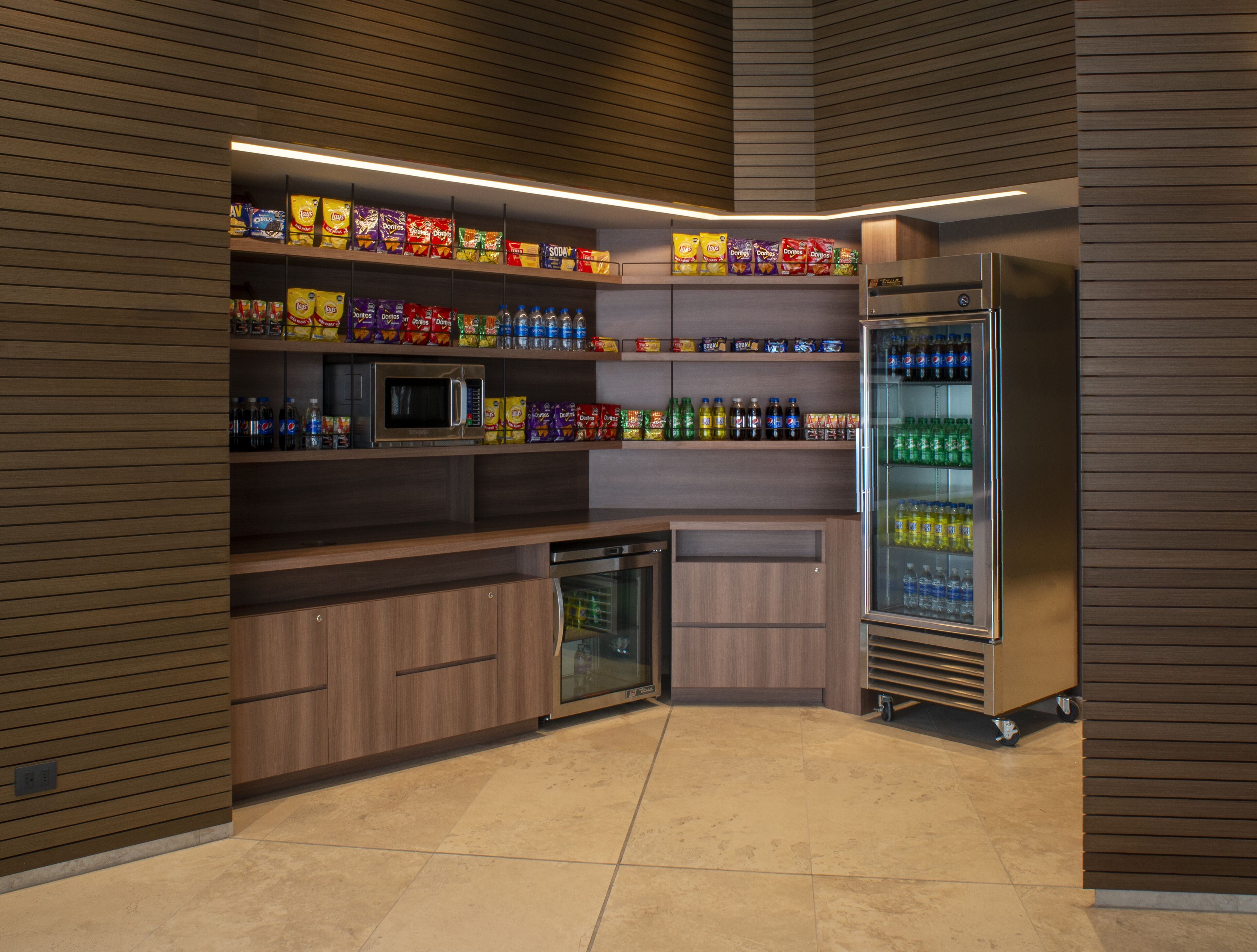 Una kitchenette equipada con microondas, refrigerador y estantes llenos de refrigerios y bebidas.
