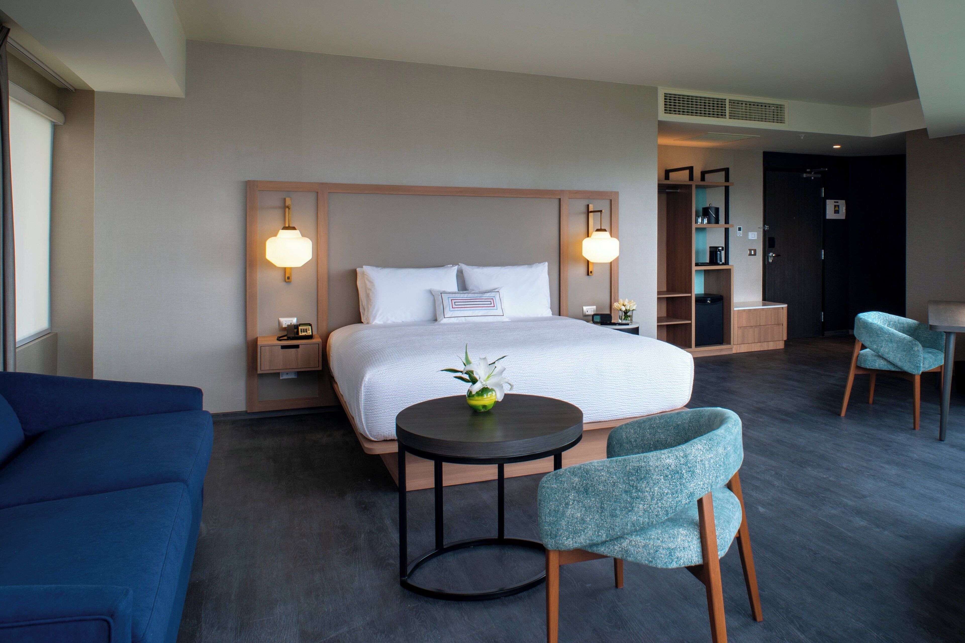 Et moderne hotelværelse med en stor seng, sengeborde, et rundt bord og to stole.