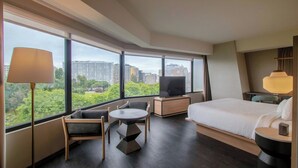 Habitación de hotel moderna con cama, televisor, escritorio y silla. Amplias ventanas con vistas a la ciudad.