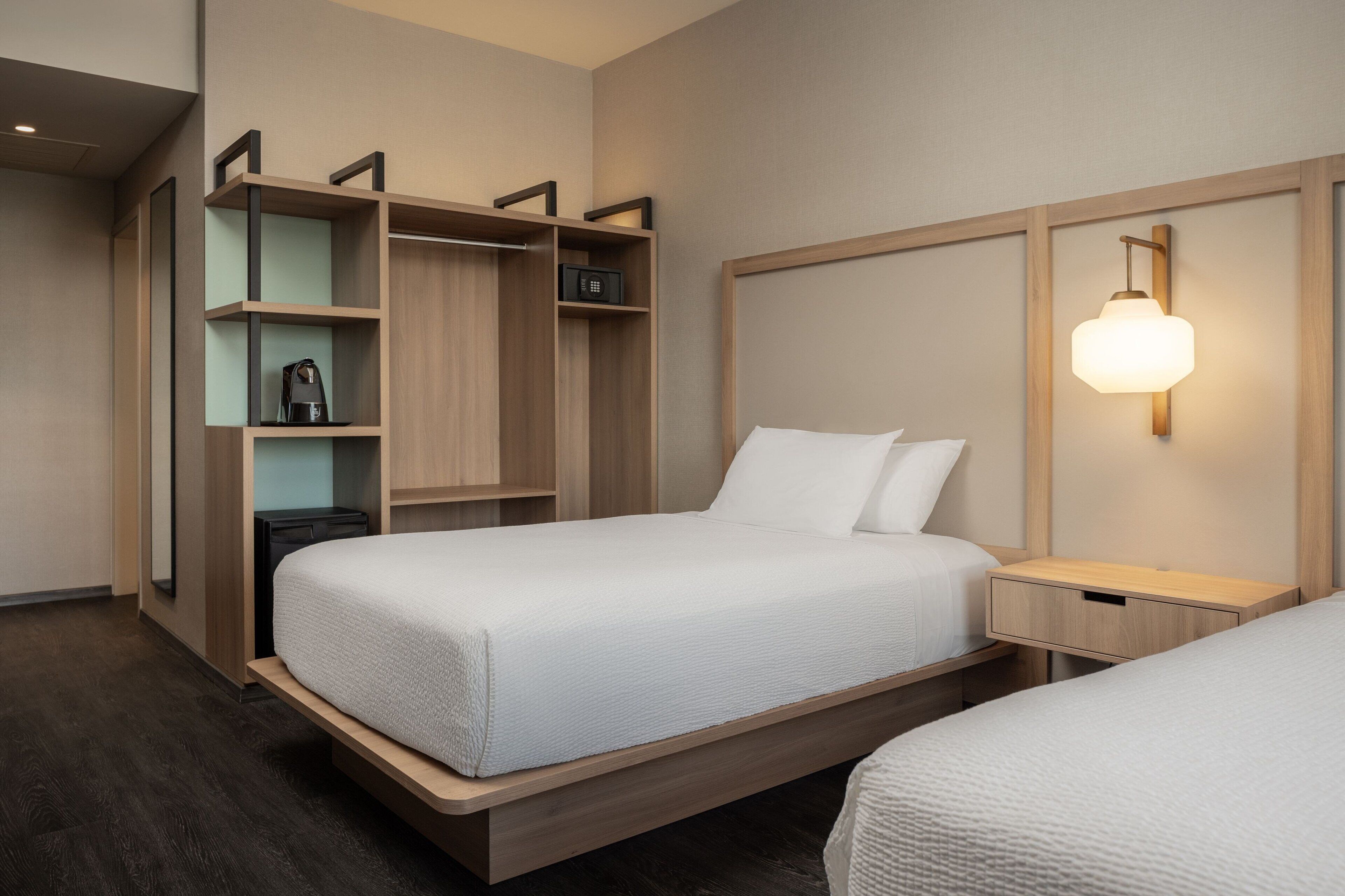 Habitación de hotel con una cama grande, una mesita de noche, un armario y una lámpara fijada en la pared.
