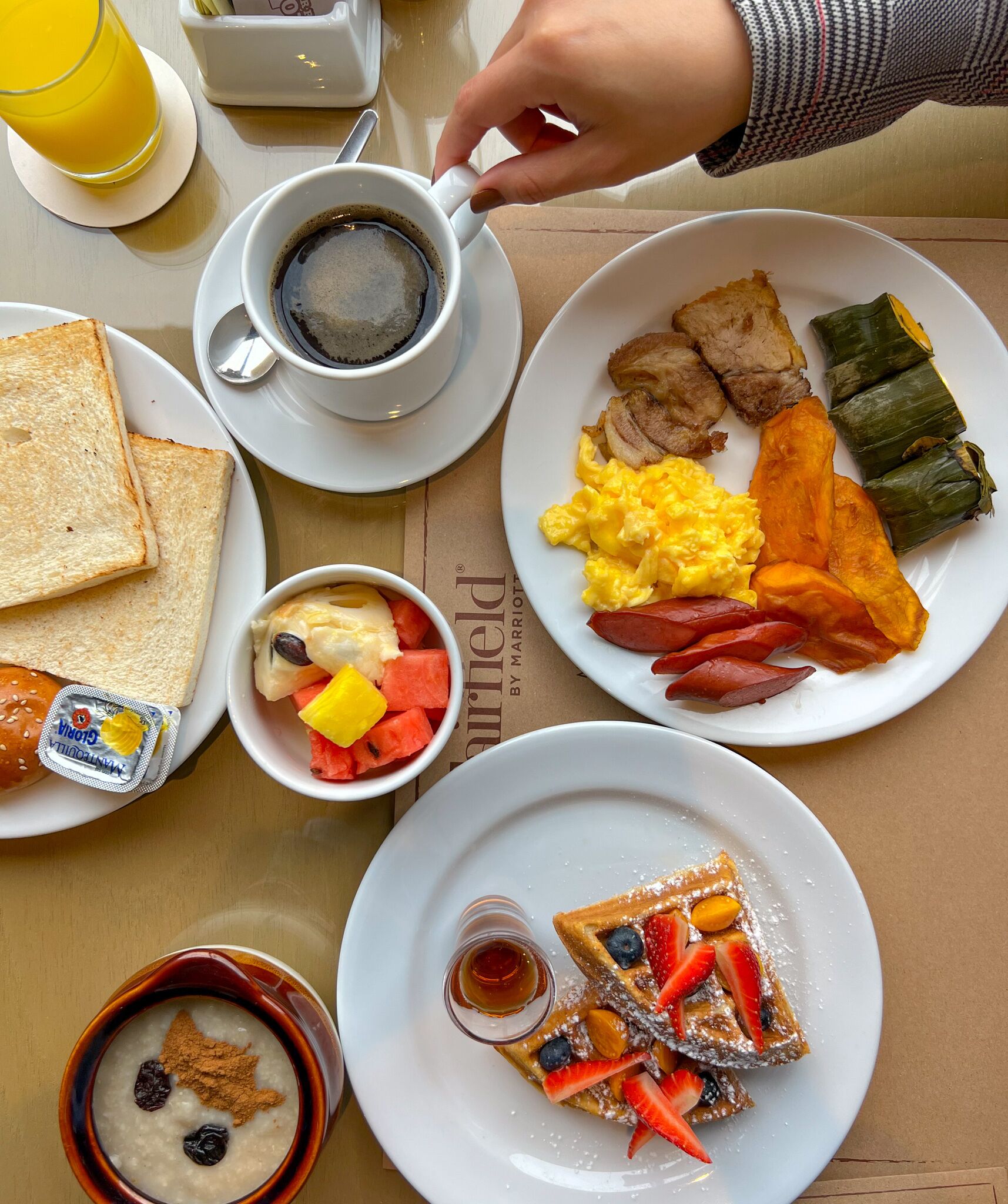 A breakfast setting with plates of eggs, bacon, toast, and a bowl of fruit.