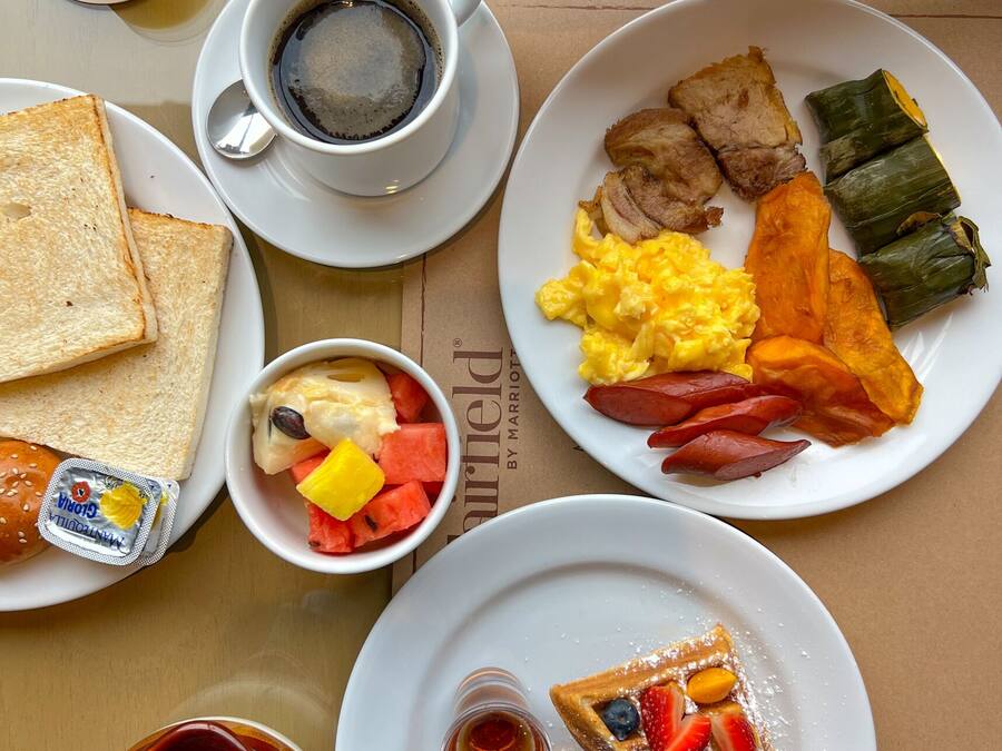 A breakfast setting with plates of eggs, bacon, toast, and a bowl of fruit.