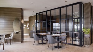 Un comedor moderno con mesas, sillas, ventanas grandes y una planta en maceta.