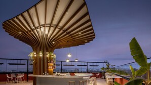 Un bar en la azotea con una estructura de techo curva distintiva, zona de bar, asientos y vistas a la ciudad.