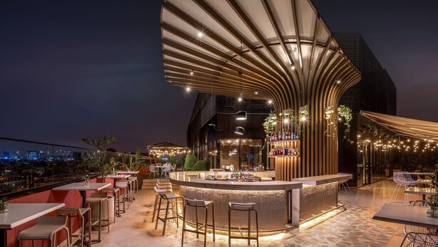 Un área de bar al aire libre con techo curvo, taburetes y mesas.