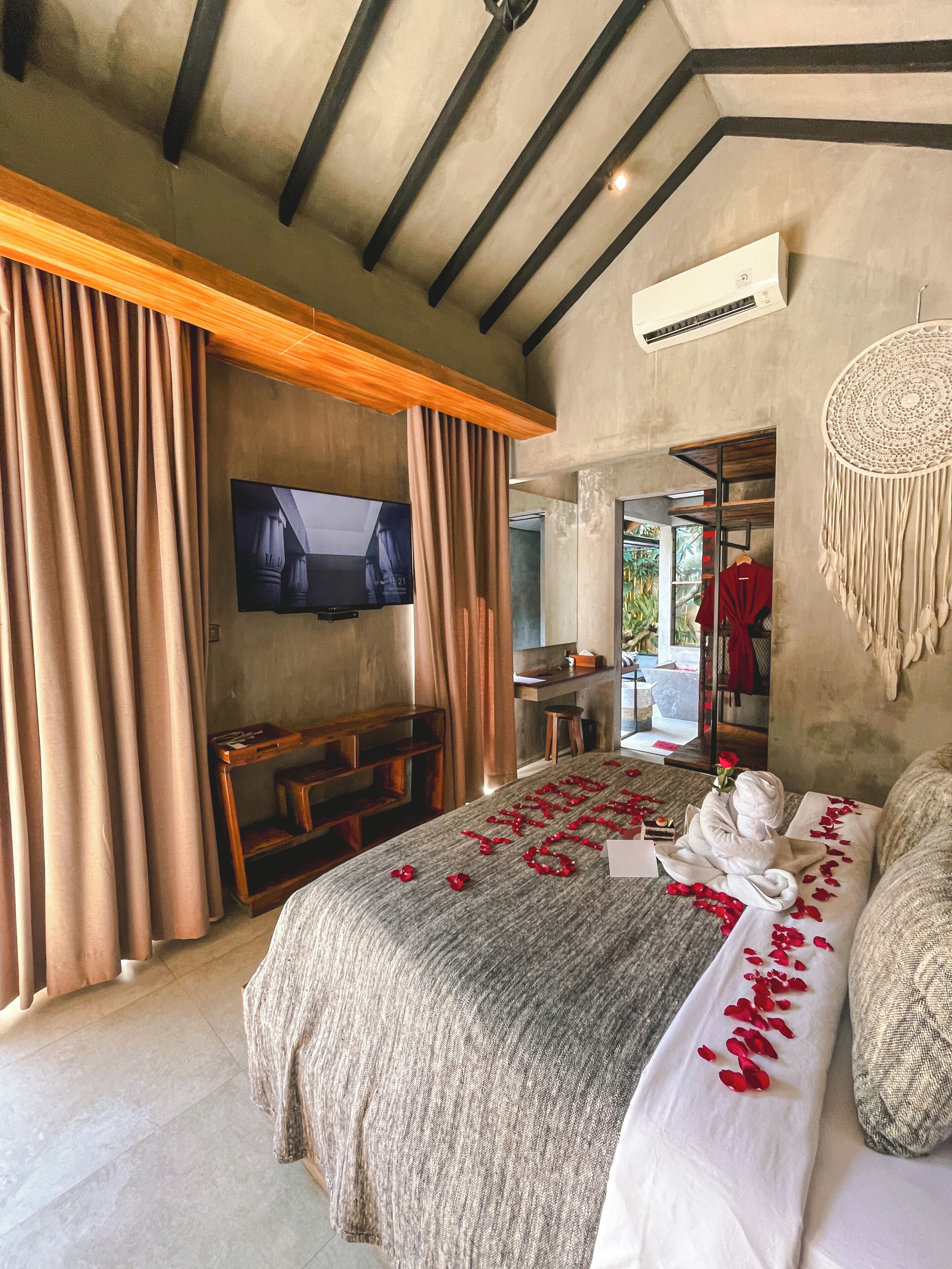 A bedroom with a large bed, a TV mounted on the wall, a desk, and a wardrobe.