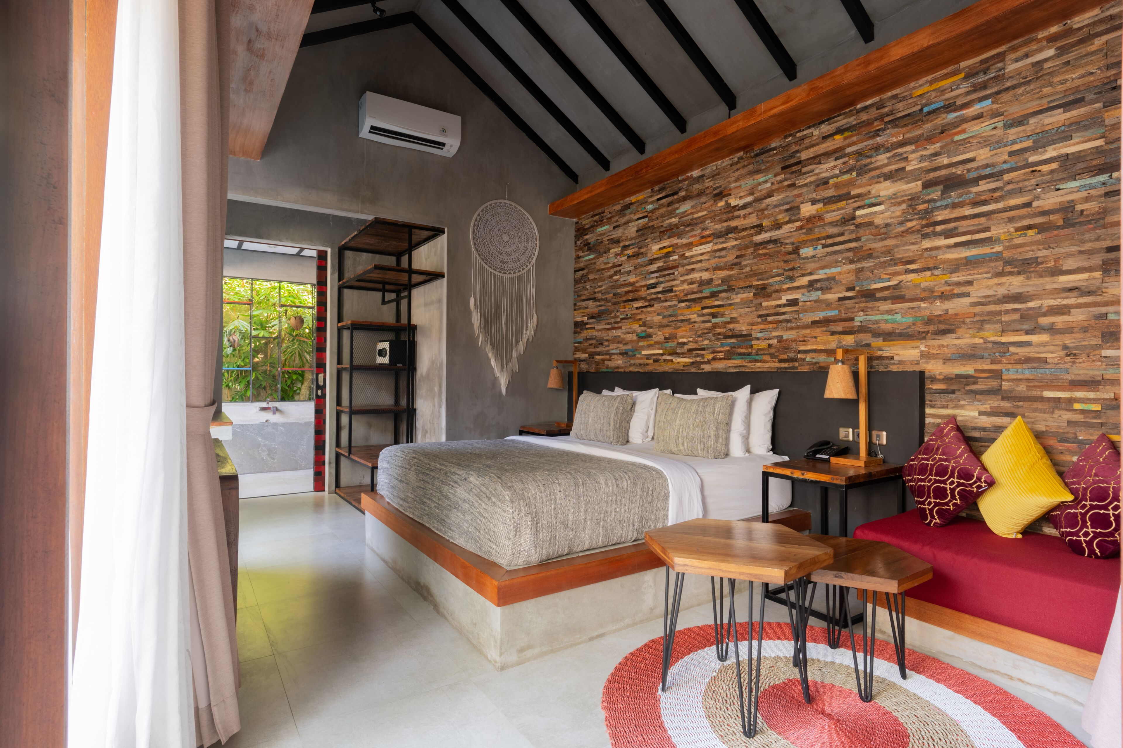 Une chambre moderne avec un grand lit, un canapé rouge, un plafond en bois et un mur en pierre.