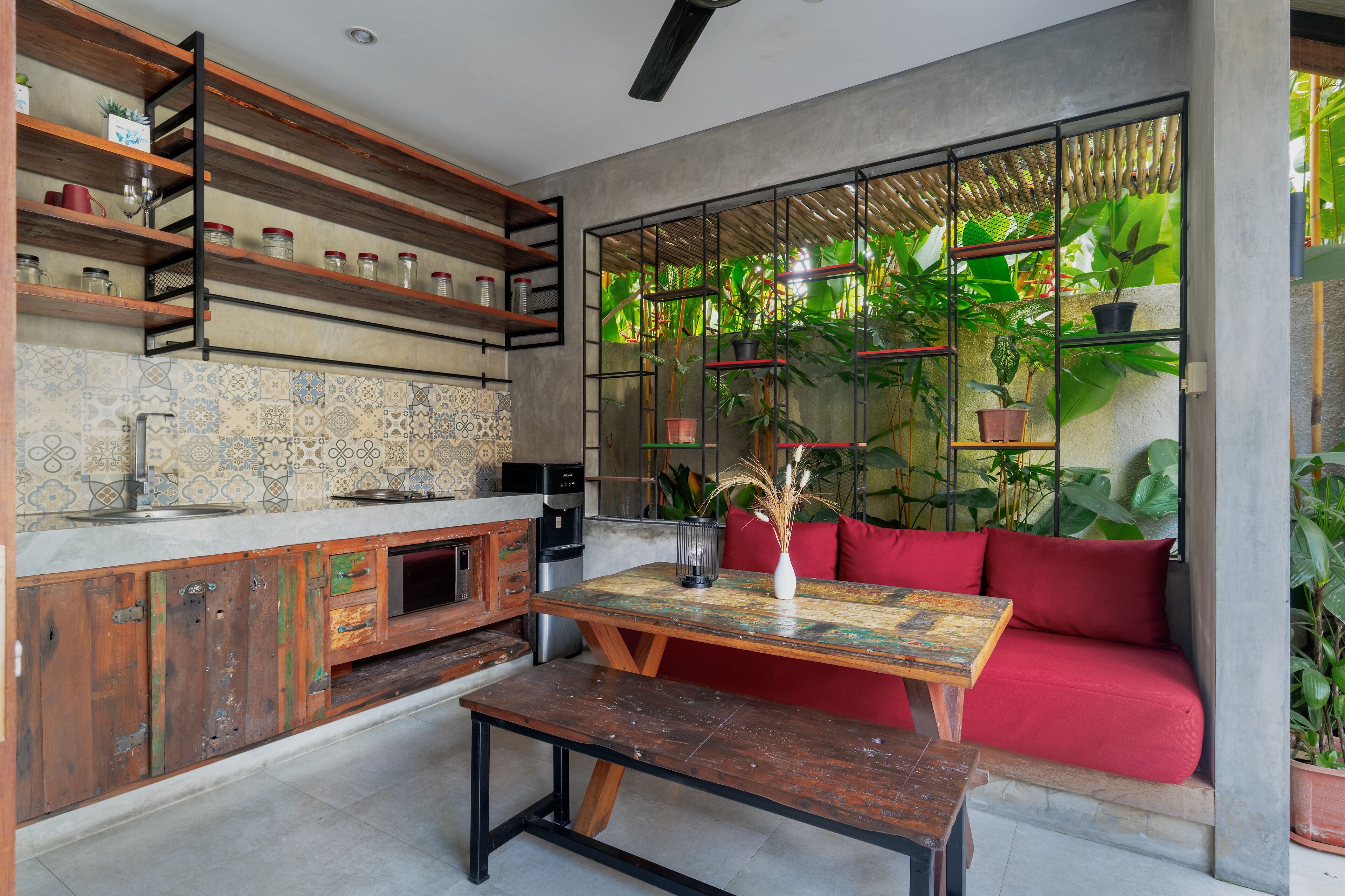 A kitchen with wooden shelves, a red sofa, and a view of lush greenery.