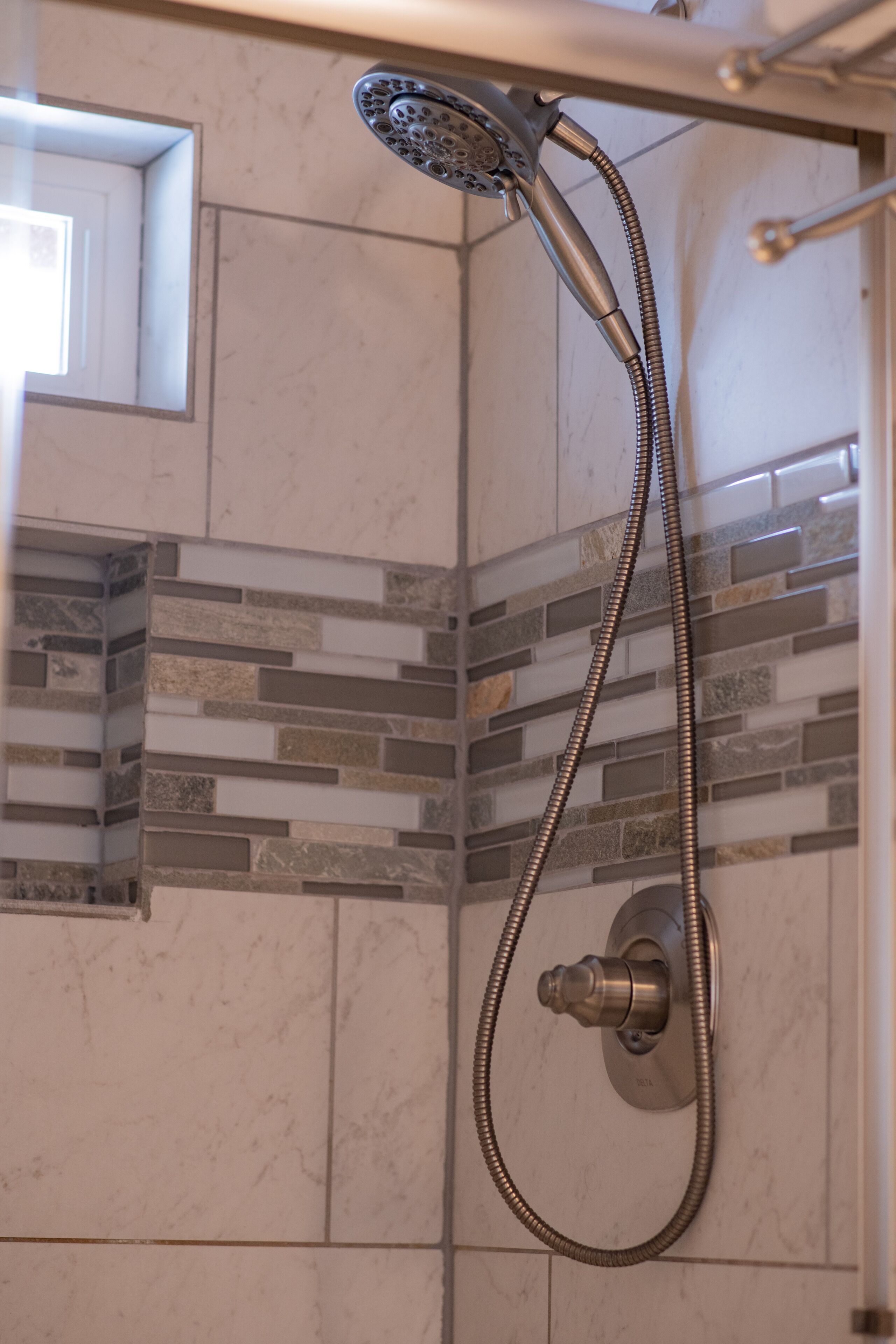 A shower with a handheld showerhead and a flexible hose, set against a wall with a mosaic tile design.