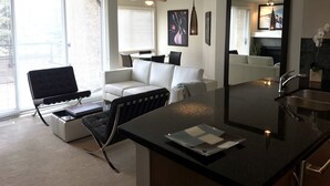 A modern living room with a sofa, a dining table, and a kitchen area with a sink and countertop. - 2 BR, 2 BA Newly Renovated Condo with Pool (Calgary)