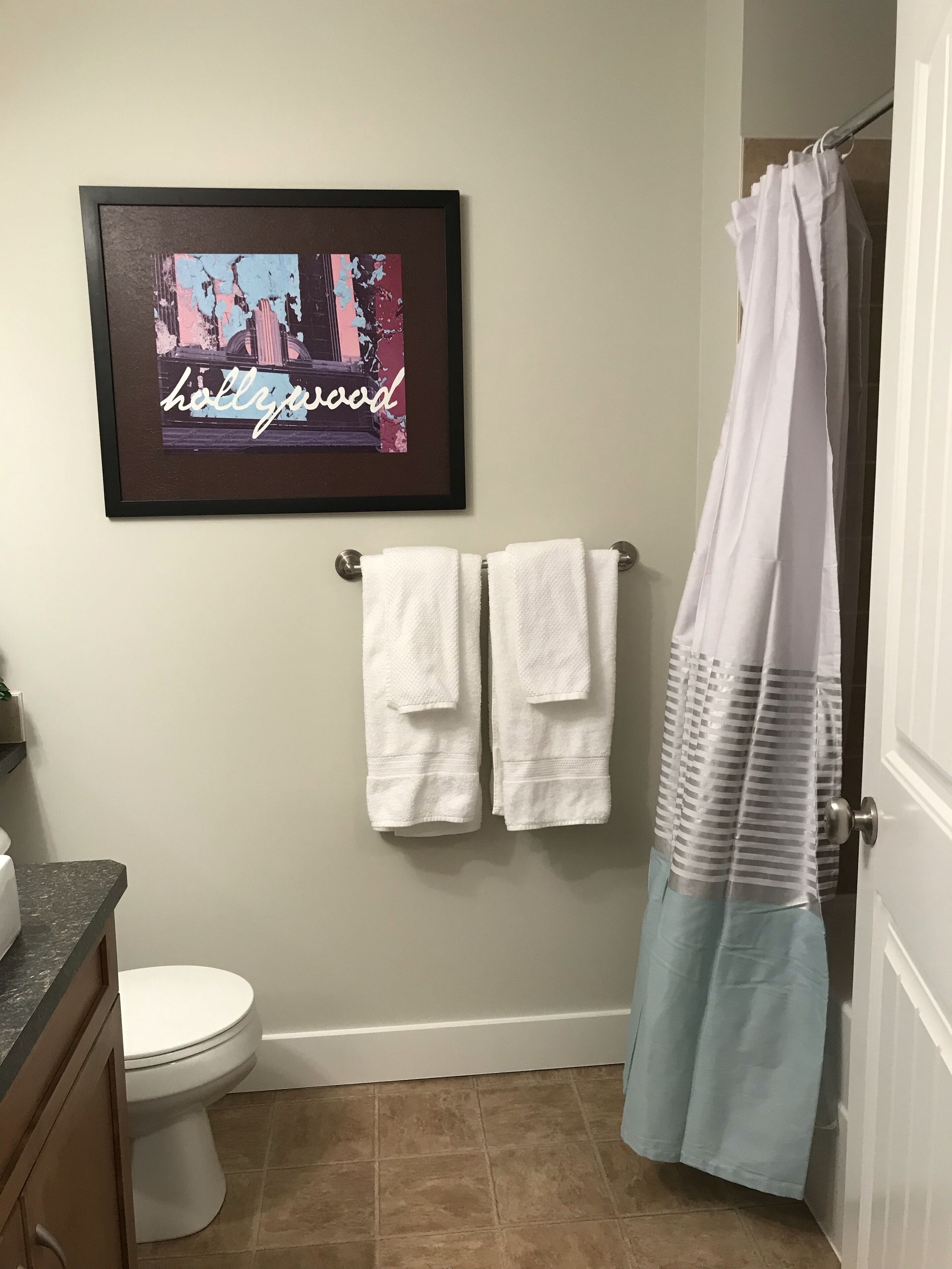 A bathroom with a framed picture, two white towels, a toilet, and a shower curtain.