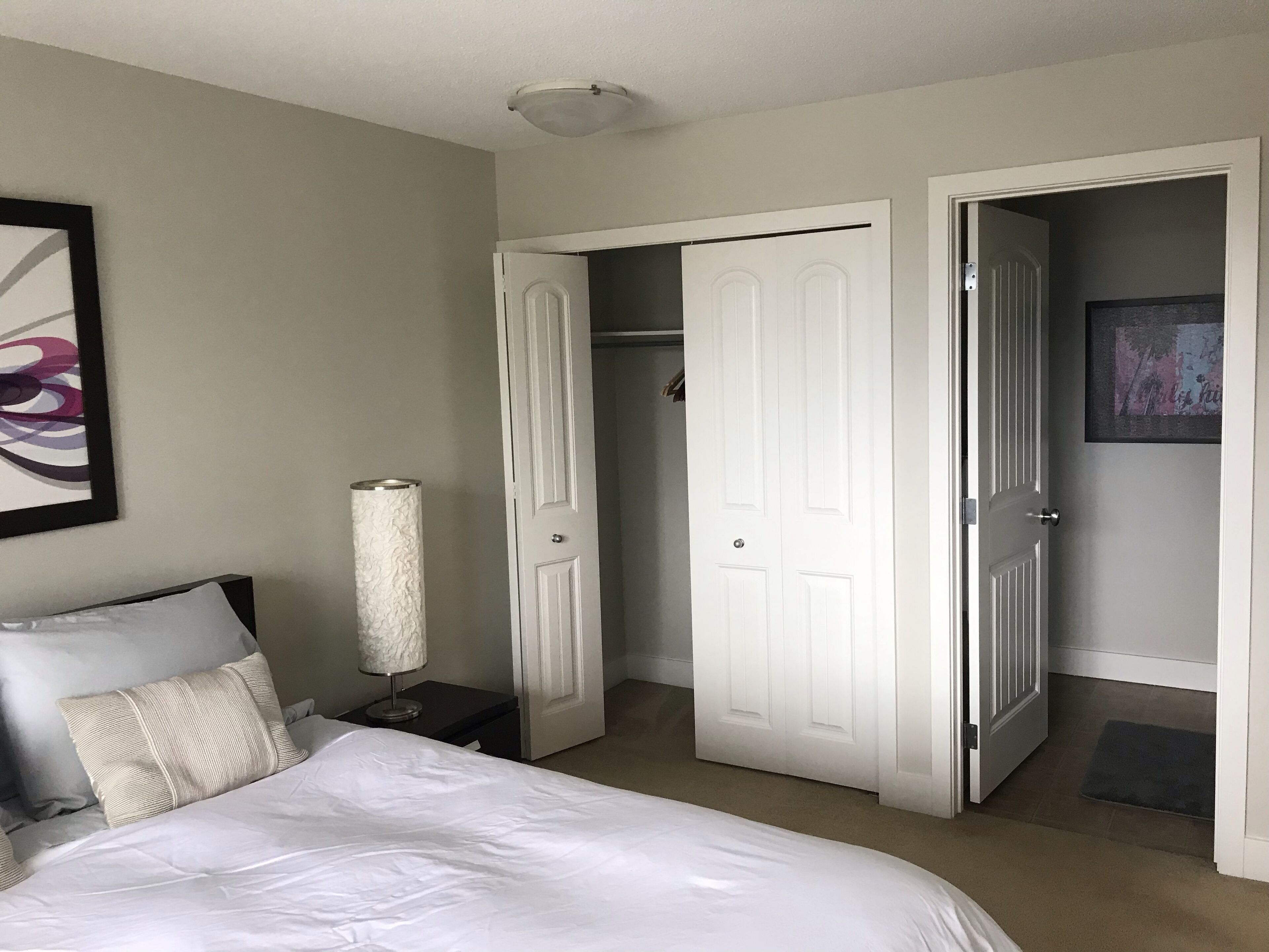 A bedroom with a bed, a nightstand, a lamp, and two doors leading to other rooms.