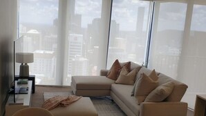 A modern living room with a large window, a beige sofa, a small table, and a lamp. - Executively Inspired - 2 Bed 2 Bath Apt on Queen St with Carpark Fast WiFi Rooftop Pool and Sleeps 5 (Brisbane City)