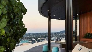 A rooftop terrace with a view of a cityscape, featuring a modern architectural design with a curved roof and a grill. - Executively Inspired - 2 Bed 2 Bath Apt on Queen St with Carpark Fast WiFi Rooftop Pool and Sleeps 5 (Brisbane City)