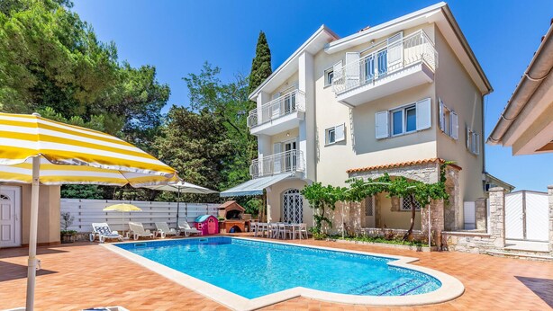 Un edificio de dos pisos con piscina, mobiliario exterior y un patio cubierto.