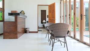 A modern kitchen with a wooden counter and a sink, a dining area with wicker chairs, and a large sliding glass door leading to an outdoor area. - Nice House Pool Villa Phuket (Chalong)