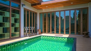 A modern pool area with a glass enclosure, wooden deck, and a view of the surrounding landscape. - Nice House Pool Villa Phuket (Chalong)