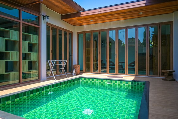 Un área de piscina moderna con cerramiento de vidrio, terraza de madera y vistas del paisaje circundante.