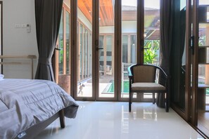 Quarto de hotel com cama, uma cadeira e vista para a área externa através de grandes portas de vidro.