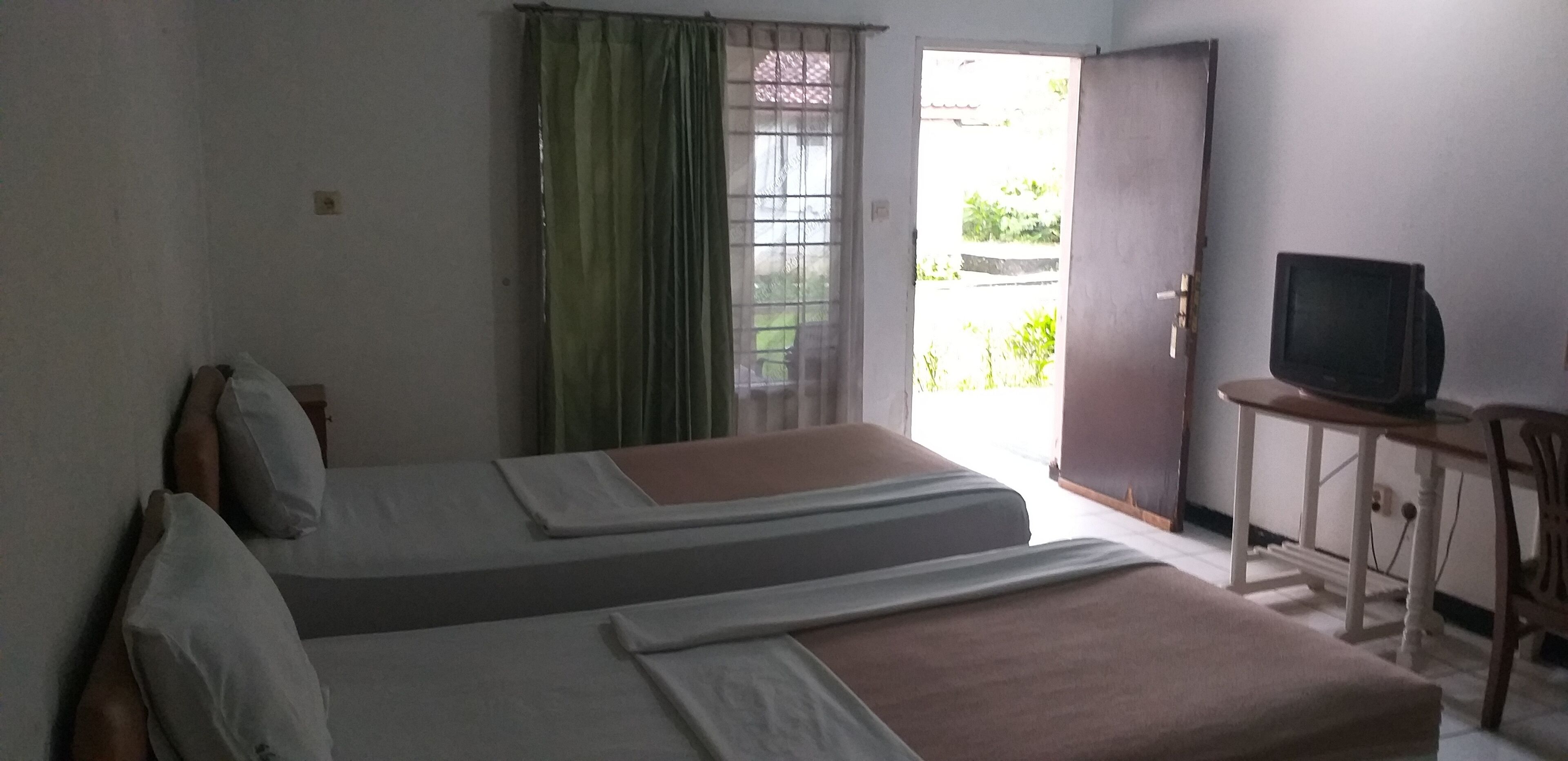 Une chambre avec deux lits, un téléviseur posé sur un bureau et une porte donnant sur un espace extérieur.