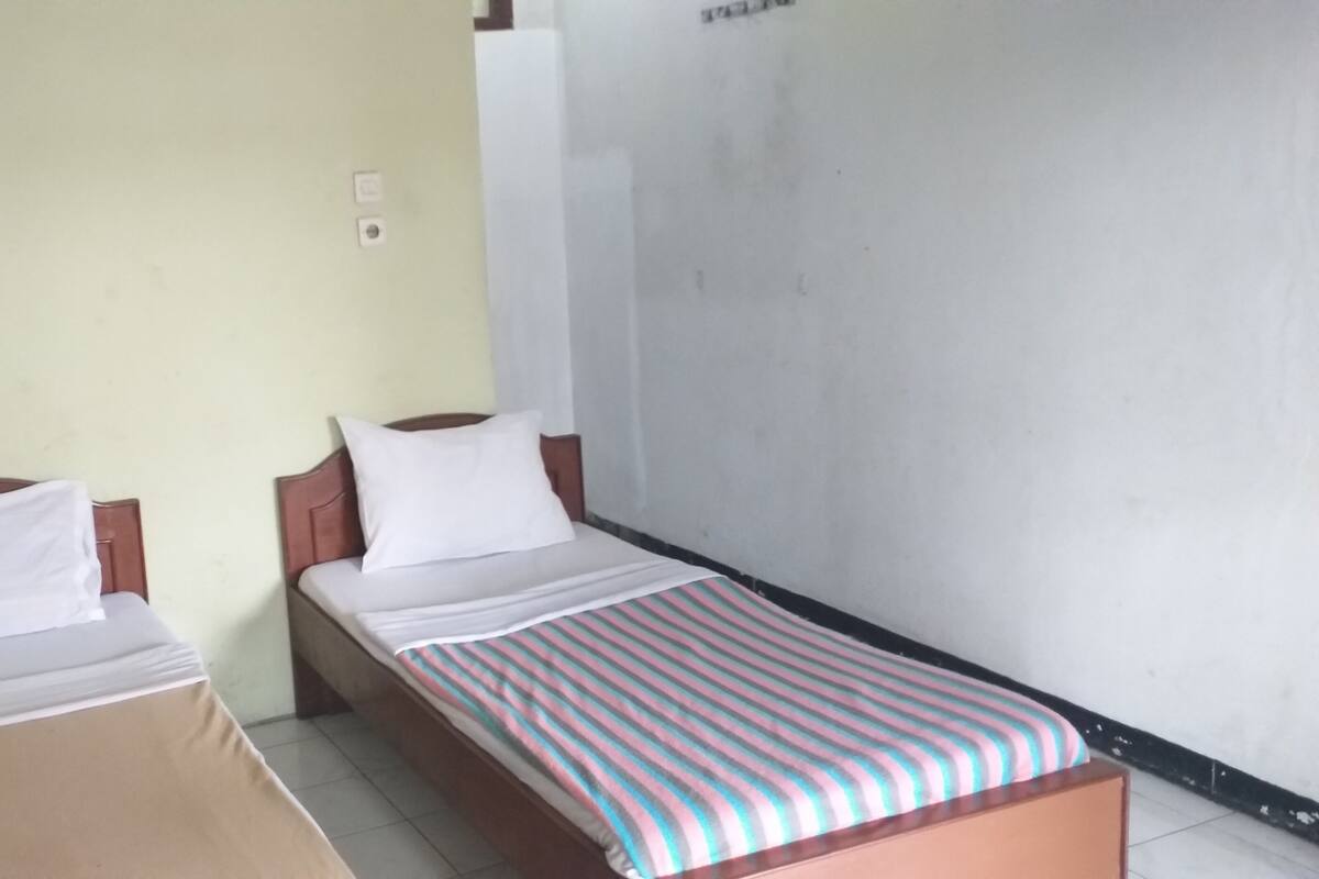 Une chambre avec deux lits simples, l’un recouvert d’une couvre-lit à rayures et l’autre d’une simple couverture blanche.