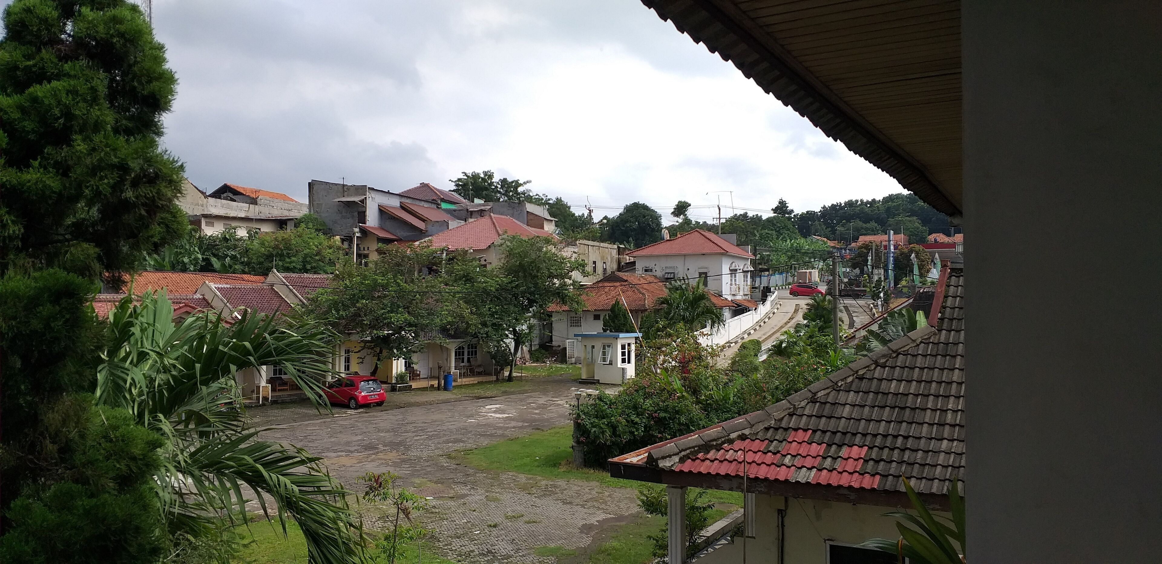 Un quartier résidentiel avec des maisons, une rue asphaltée et une voiture rouge garée sur le bord.
