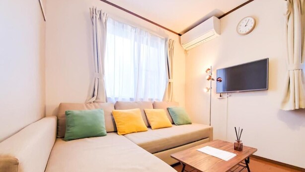 A modern living room with a sofa, a coffee table, a flat-screen TV, and an air conditioning unit. - Nestay Suite Tokyo Shibuya (Tokyo)