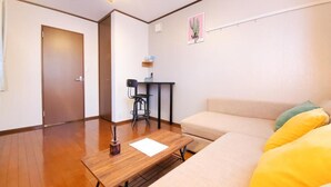 A living room with a wooden floor, a sofa, a small table with a chair, and a door. - Nestay Suite Tokyo Shibuya (Tokyo)