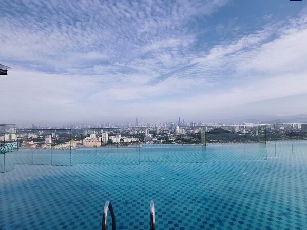 An infinity pool with a cityscape view, metal pool ladder, and a clear sky.