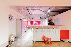 A modern interior with a central reception desk, pink lockers, and decorative elements like a clock and a small elephant statue. - Nikko Inn Minamisenba - Hostel (Osaka)