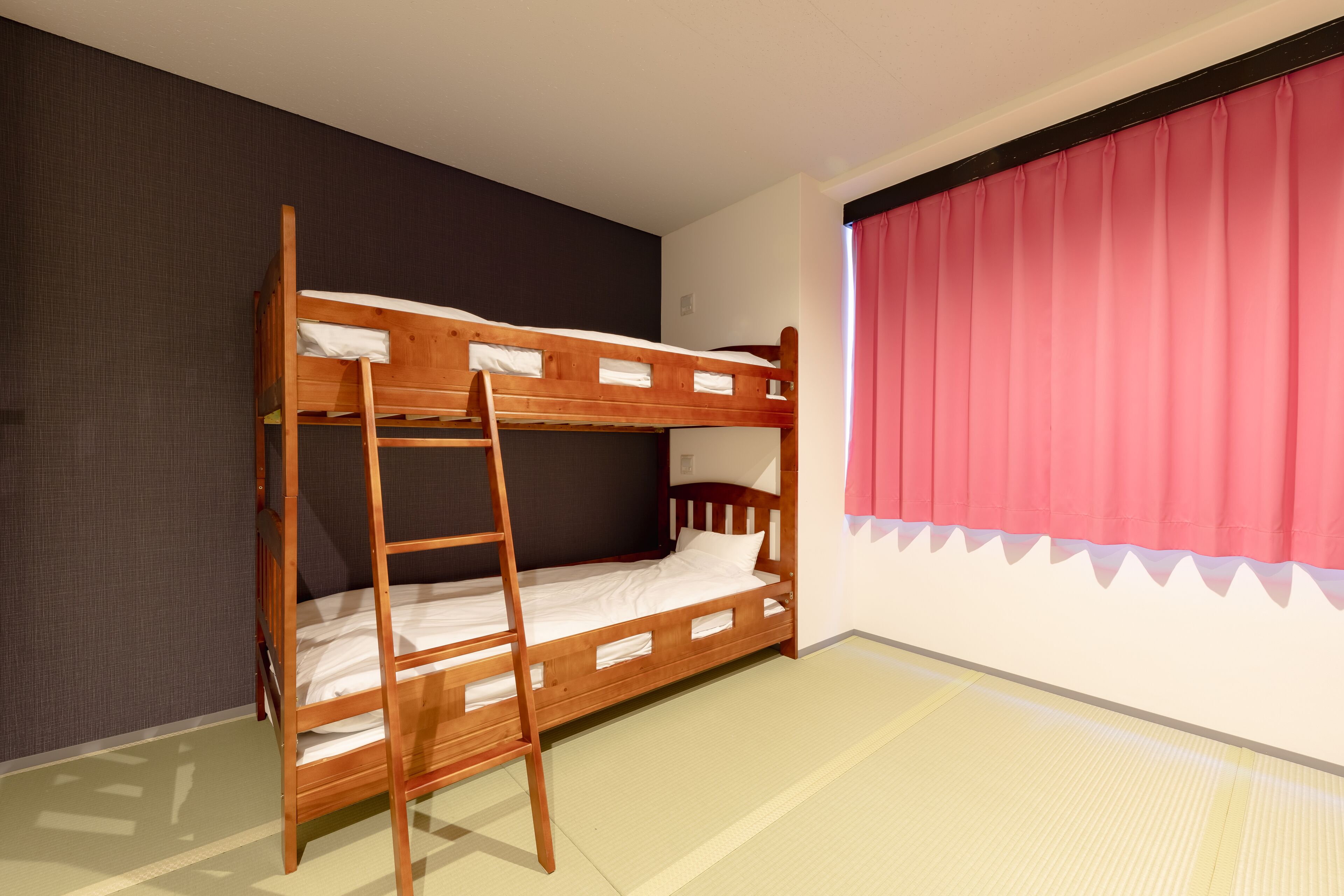A bunk bed room with a ladder, a window with pink curtains, and a dark wall.