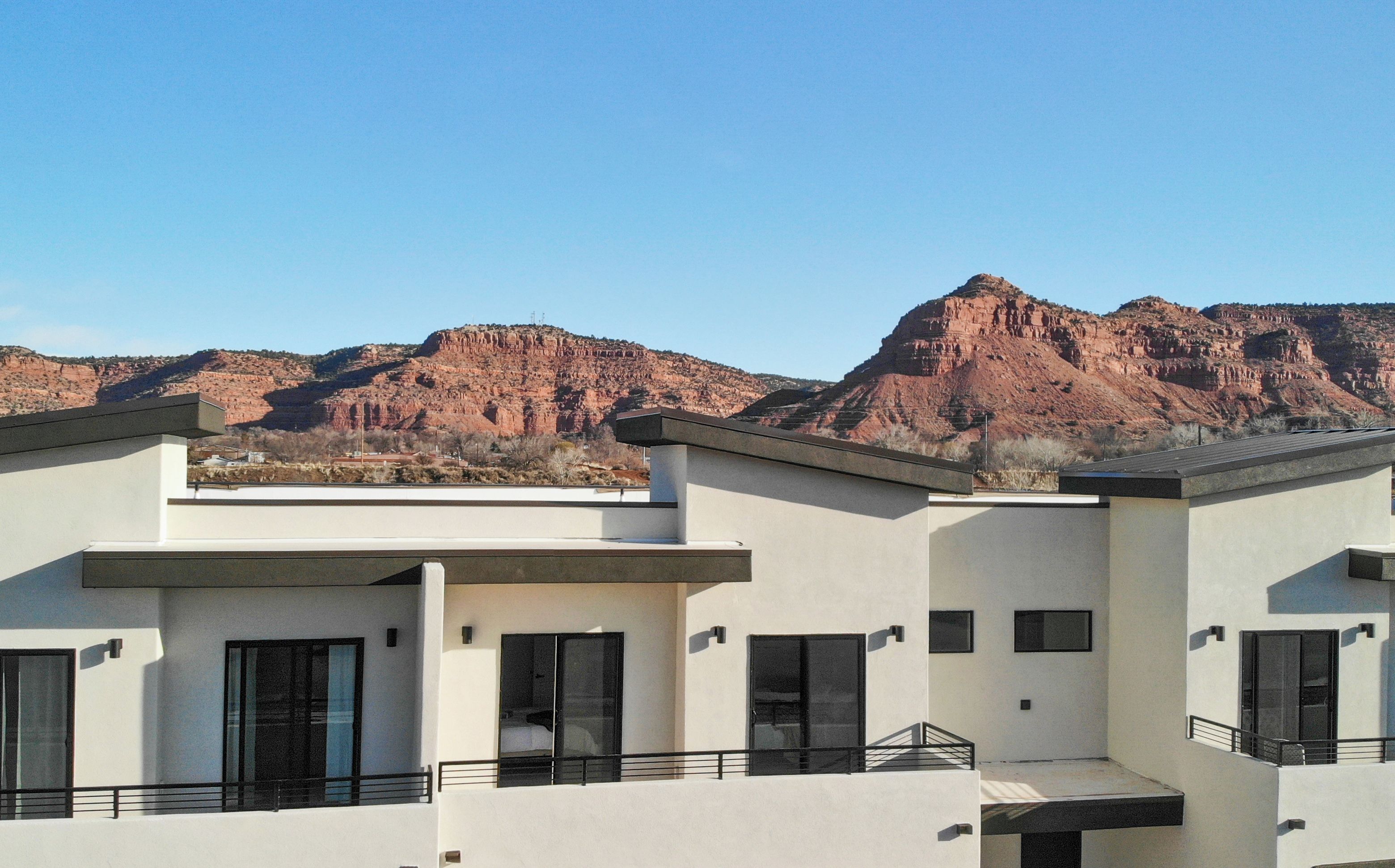 A modern multi-story building with a flat roof and large windows, set against a backdrop of red rock formations.