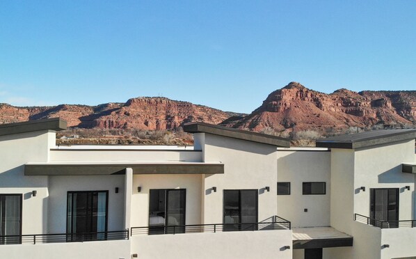 A modern multi-story building with a flat roof and large windows, set against a backdrop of red rock formations. - Grand Circle GetAway at Crimson Rocks (Kanab)