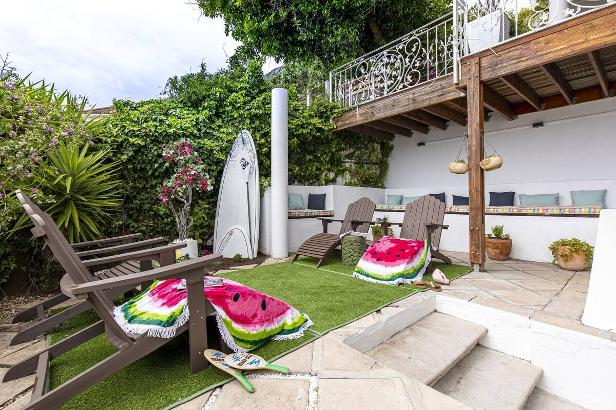 Eine Terrasse mit einer Holzbank, einem Surfbrett und einer Decke mit Wassermelonenmuster.