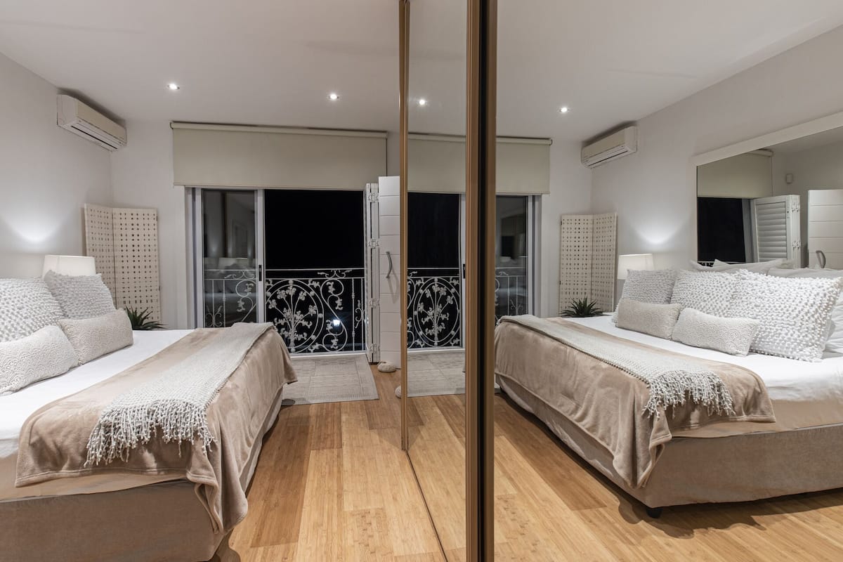 Ein Schlafzimmer mit Spiegel, zwei Betten, einem Balkon mit Geländer und Blick auf den Nachthimmel.