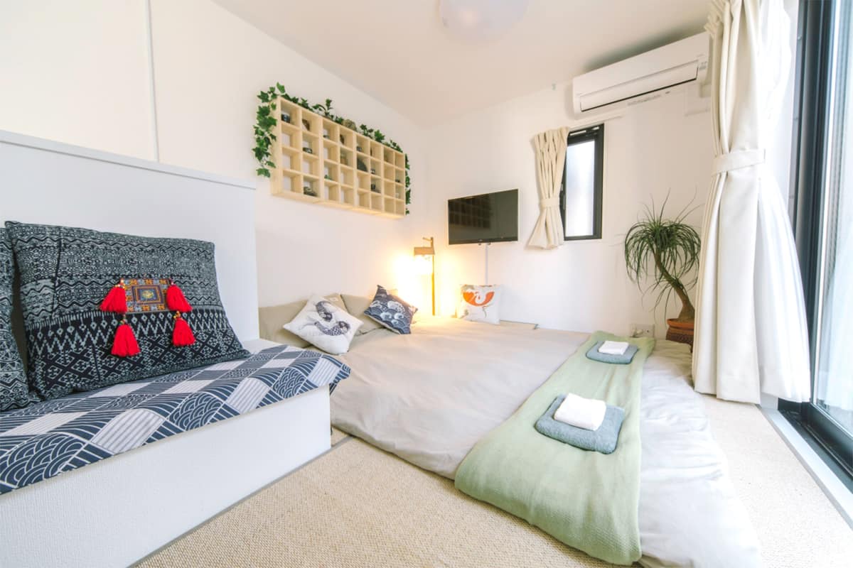 A modern bedroom with a sofa, two beds, a TV, a wall-mounted shelf with plants, and a potted plant by the window.