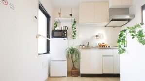 Eine kompakte Küche mit weißen Schränken, einer Mikrowelle, einem Kühlschrank und einem Blumentopf.