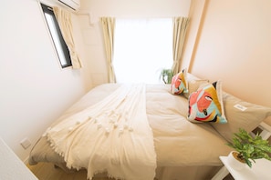 Un dormitorio con cama, ventana, cortinas, una planta y una mesita de noche.