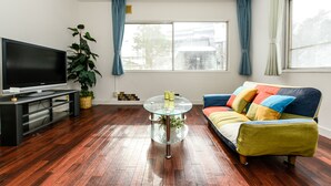 Un salon doté d’un téléviseur à écran plat, d’une table basse en verre, d’un canapé coloré et d’une grande fenêtre agrémentée de rideaux.