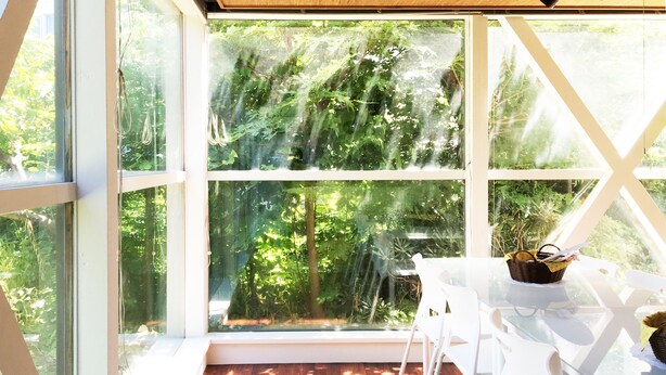 Une véranda avec un plancher en bois, des chaises blanches et une table sur laquelle se trouve un panier.