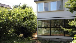 Une maison moderne à deux étages, dotée de grandes fenêtres et d’un jardin.