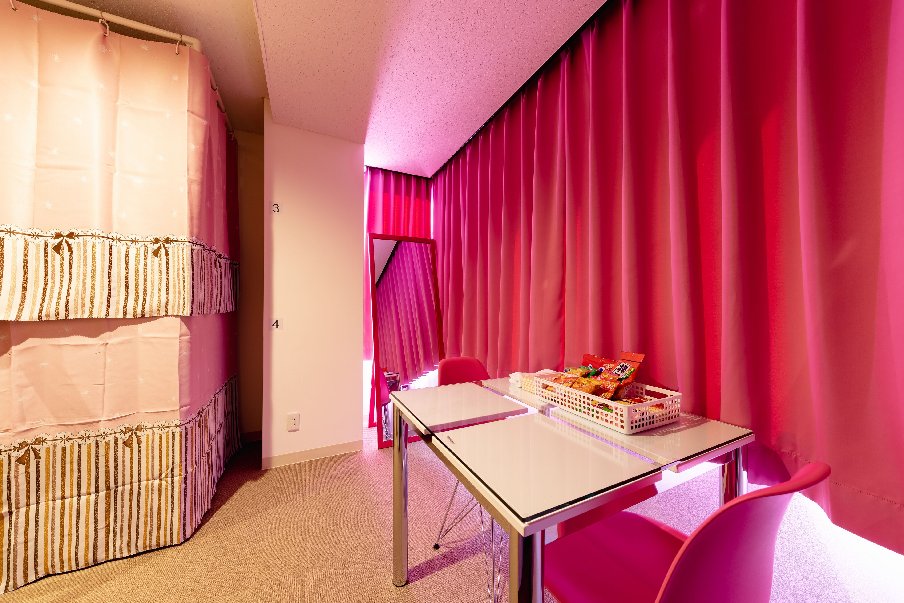 A room with a bunk bed, a table with a basket of snacks, and a red curtain.