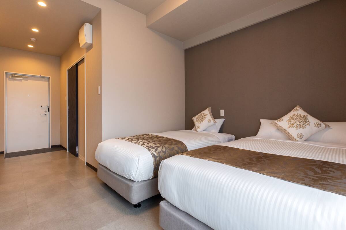 A hotel room with two beds, a door, and a wall-mounted air conditioner.
