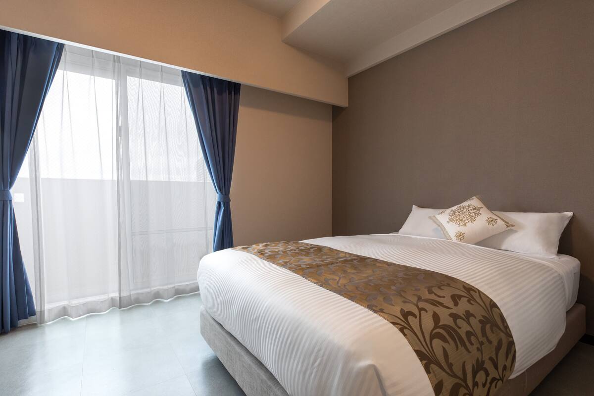 A hotel room with a large bed, a window with sheer curtains, and a view of the outdoors.